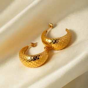 Detailed close-up of 18k gold fish scale earrings on elegant silk background