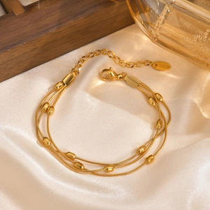 Three-layer gold stainless steel chain bracelet with metallic beads on white satin