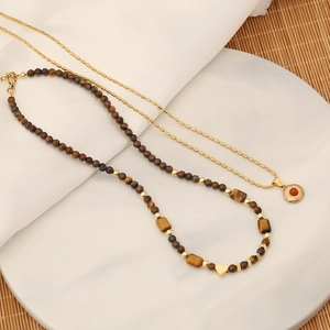 Macro shot of tiger eye beaded necklace with gold heart pendant on white marble tray