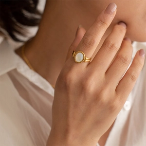 Elegant gold ring with oval white mother of pearl shell worn by a woman in white shirt