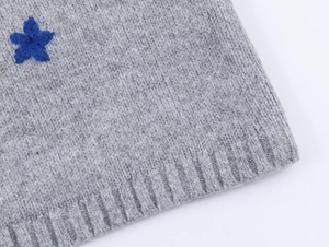 Close-up of grey knit cardigan detail with blue flower embroidery and ribbed cuffs