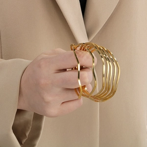 Close-up of stacked wavy gold bangles in polished stainless steel on a blazer sleeve