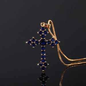 Close-up of golden cross pendant with deep blue crystals and shimmering starburst details