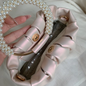 Macro view of pearlescent pink cloud handbag featuring a pearl handle and gold clasp
