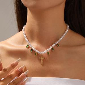 Elegant gold-plated pearl necklace with green square gems and a cross pendant on model
