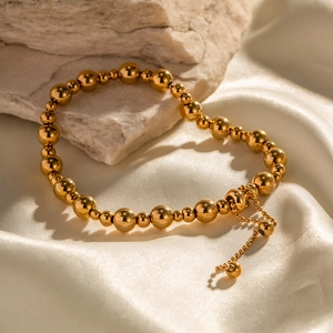 Detail eines verstellbaren Goldperlenarmbands auf weißer Seide und Naturstein