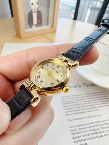 Close-up of golden vintage quartz watch with Roman numerals and black leather strap