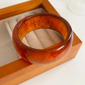 Macro view of amber resin bangle with marbled texture displayed on a wooden jewelry box