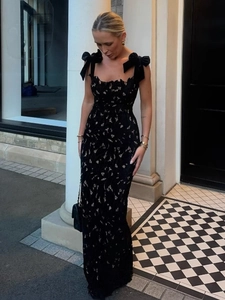 Elegant black lace maxi dress featuring oversized bow shoulder straps in a city setting