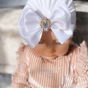 Detail of baby turban featuring a large white satin bow with a decorative opal gemstone