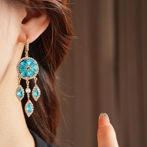 Close-up of vintage gold earrings with blue gemstones and sparkling zircon fringe