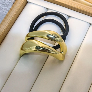 Macro detail of wave-shaped golden metal hair ring with black elastic on jewelry tray
