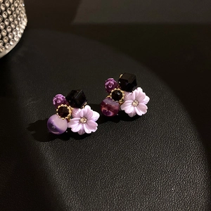 Detailed view of purple flower earrings with faux crystals on black leather background