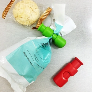 Detail view of red and green plastic food clips sealing a snack bag on a grey surface