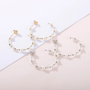 Close-up of gold and silver C-shaped earrings with white pearls on a soft background