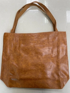 Gros plan détaillé sur la texture du cuir huilé brun et les anses de ce sac cabas