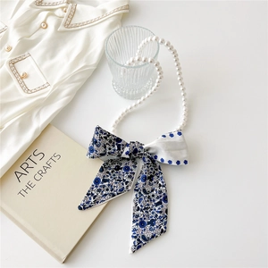 Detailed shot of pearl necklace with blue floral silk ribbon bow on art book background