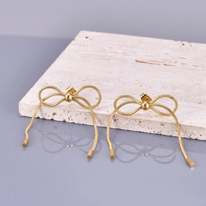 Detail of 18K gold bow stud earrings with sleek snake chain tassels on a stone surface