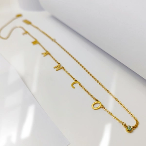 Detalle de collar dorado con letras TITANCO y gema de piedra de nacimiento verde