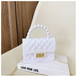Close-up of white quilted jelly bag with pearl handle and golden chain on a book