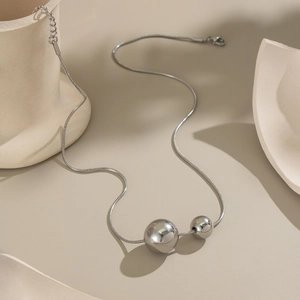 Detailed view of silver snake chain necklace featuring double sphere pendants on a beige base