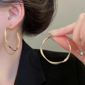 Detailed close-up showing the golden twisted hoop earring texture and glossy metallic finish