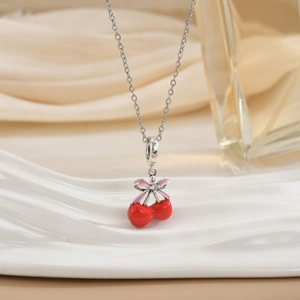 Close-up of a silver necklace with red cherry pendant and a pink bow on fabric