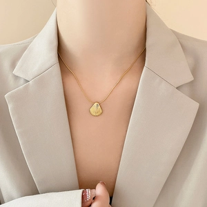 Elegant gold shell pendant on snake chain necklace worn by a model in a beige blazer