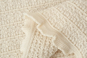 Vue macro d'un tissu tricoté blanc cassé montrant la texture fine et le bord ondulé