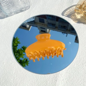 Detail of a translucent bright orange claw clip on a mirror reflecting the blue sky