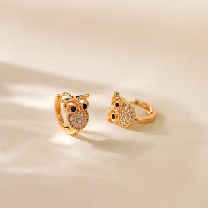 Exquisite 18K gold plated owl earrings with sparkling cubic zirconia on beige fabric
