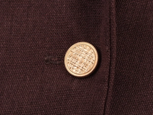 Close-up of golden embossed button on dark brown knitted fabric blazer sleeve