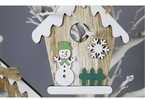 Detail of wooden Christmas cottage ornament with snowman and fence on tree branch