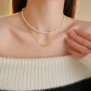 Close-up of layered necklace with white pearls and a gold-tone snake chain on a model