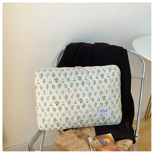 Detail of floral quilted laptop sleeve in off-white fabric with zipper and woven label