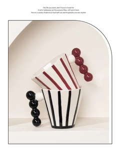 Close-up of retro ceramic mugs with vertical stripes and artistic beaded handles on a shelf