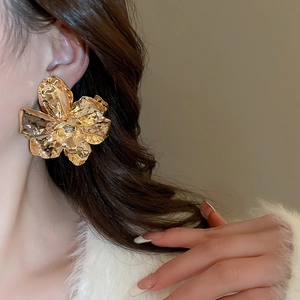 Close-up of a large gold petal earring with a 3D folded texture on a model's ear