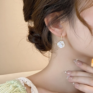 Detail view of a model wearing camellia flower earrings with gold edges and small diamonds