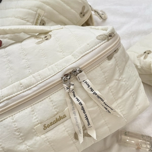Detail of soft cream quilted fabric cosmetics bag with cute rabbit embroidery and brand tag
