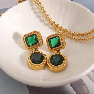 Detailed close-up of retro gold-plated earrings with emerald green zircon in ceramic dish