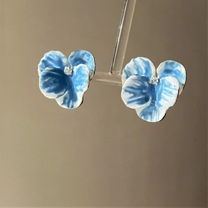 Macro shot of blue pansy flower stud earrings with a sparkling crystal center