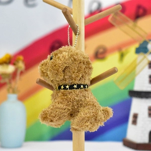 Detail view of a cute brown plush teddy dog keychain hanging on a wooden display stand.