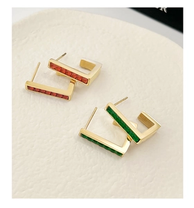 Macro detail of geometric gold metal earrings featuring red and green square gemstones