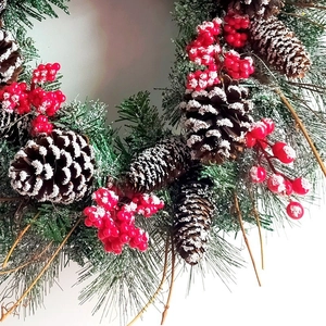 Christmas wreath with green pine needles, brown cones, red berries and snow effect