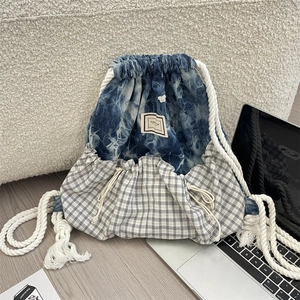 Detail of blue denim and plaid patchwork backpack with white cotton drawstring and label