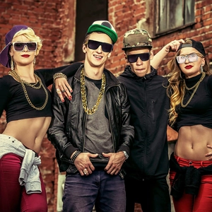 Hip hop style gold chain necklace and sunglasses worn by model against red brick wall