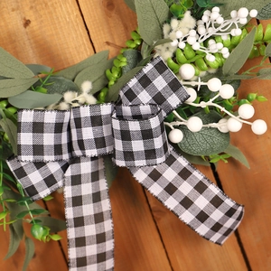 Artificial white berry and willow leaf wreath with buffalo plaid bow on wooden background