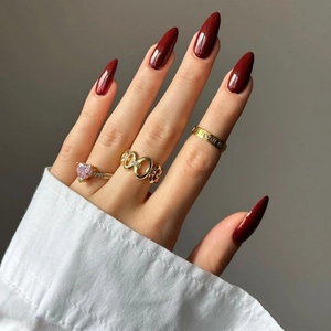 Golden ring set with pink heart gemstone and chain design on wine red manicured nails
