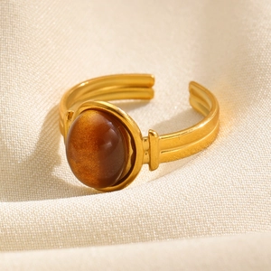 Detail of adjustable gold ring with oval brown gemstone on a textured linen fabric