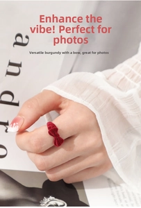 Detail of a burgundy velvet bow-shaped ring worn on a finger with white lace cuff
